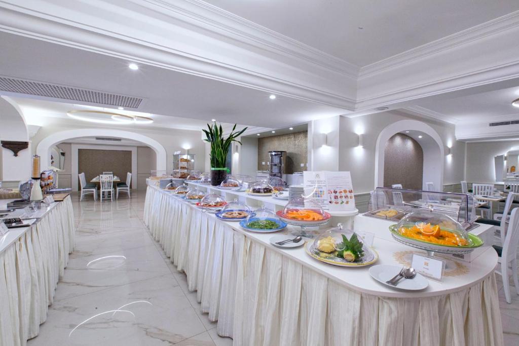 Bagātīgs bufete ar dažādiem ēdieniem un augļiem, kas pasniegti modernā restorāna vidē. Gaisīgs interjers ar elegantu galdu noformējumu.