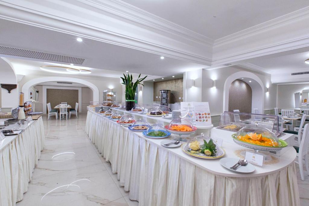 Bagātīgs bufetes galds ar dažādiem ēdieniem un salātiem, kas izvietoti elegantā restorānā. Galds rotāts ar augiem un ir pieejami daudzi ēdieni.