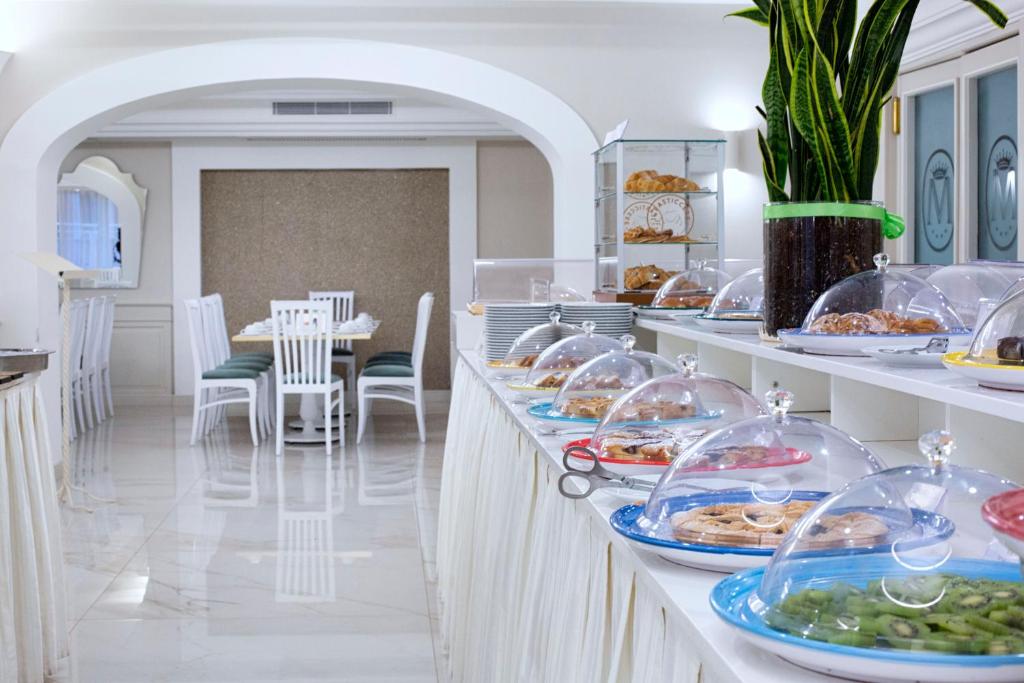 Brokastu bufete ar dažādiem ēdieniem, kas pasniegti zem caurspīdīgām vāciņām, un elegantām baltām mēbelēm. Interjers ir gaišs un mūsdienīgs, radot patīkamu atmosfēru.