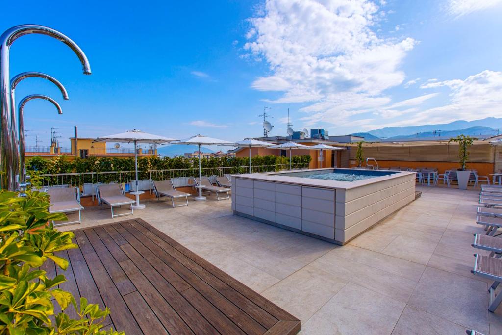 Lieliska skatu uz jumta terasi ar baseinu, sauļošanās krēsliem un sauļošanās lietussargiem, apkārt ir zaļumi un kalnu ainava.