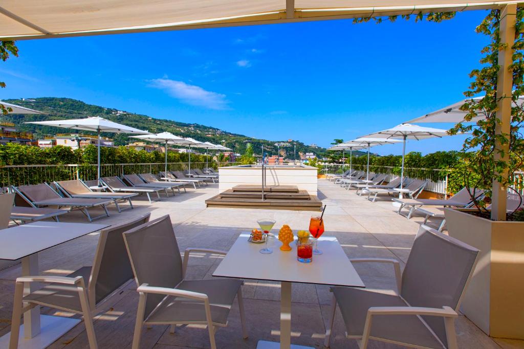 Saulaina terase ar sauļošanās krēsliem un kokteiļiem, kas atrodas viesnīcā, ar skatu uz kalniem un zilo debesu fonu. Ideāla vieta relaksācijai un atpūtai.