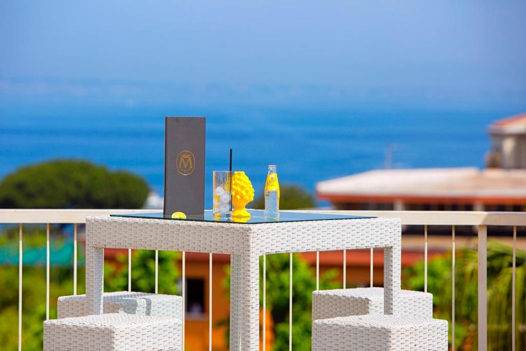Terases galdiņš ar dzērieniem un ēdienu sarakstu, fons ar jūras skatu un saulainu debesi.