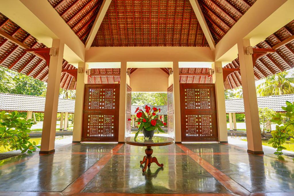 Mūsdienīgs un stilīgs viesnīcas vestibils ar augstiem griestiem un dekoratīviem koka durvīm, centrā ziedu kompozīcija uz galda. Apgaismojums rada viesmīlīgu atmosfēru.