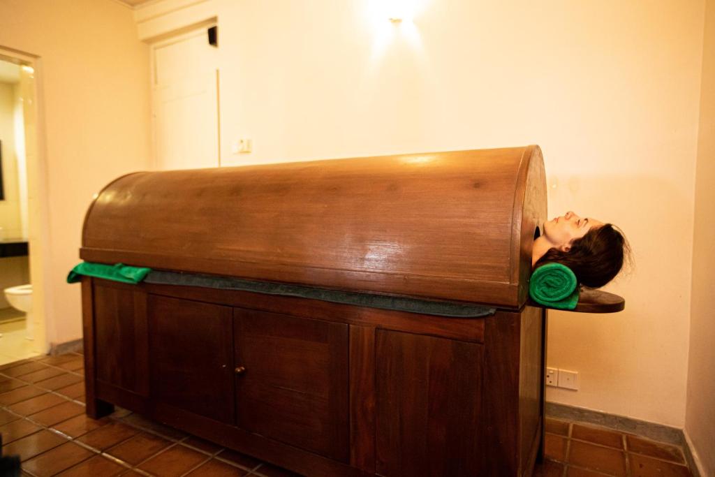 Koka tvaika pirts ar cilvēku, kurš guļ iekšā, izceļo relaksācijas un labsajūtas vidi. Zaļi dvieļi uz pirts malas piešķir viesmīlīgu pieskārienu.