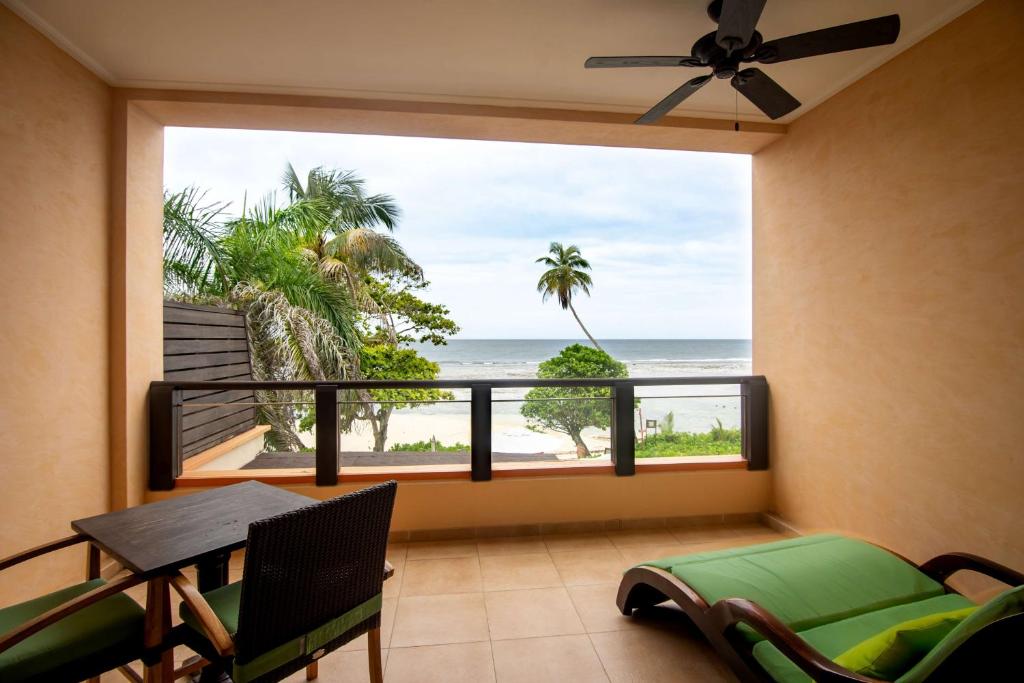 Terases skats uz pludmali, kur redzami palmas un jūra, ar zaļu atpūtas krēslu un galdu.