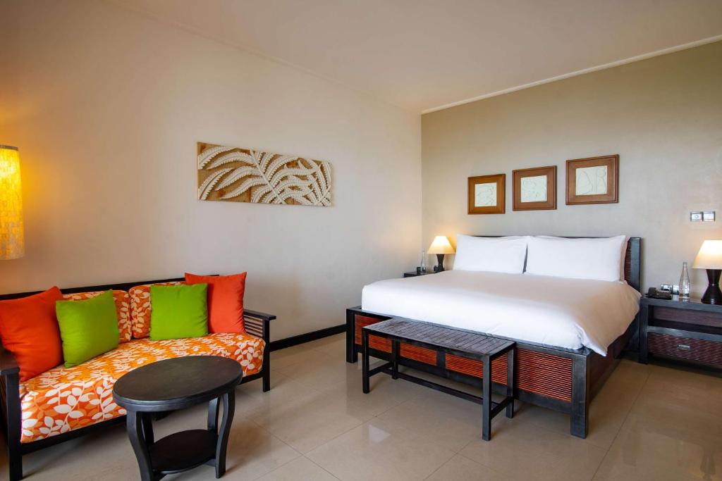 Mūsdienīgs viesnīcas numurs ar ērtu divguļamo gultu un komfortablu atpūtas zonu, kurā ir spilgti dīvāni un kafijas galdiņš. Interjers ir gaišs un elegants, radot patīkamu atmosfēru.