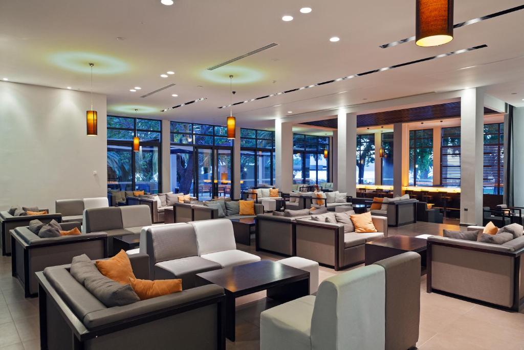 Mūsdienīgs viesnīcas interjers ar ērtām dīvānu zonām un lieliem logiem, kas nodrošina dabīgu apgaismojumu un skatu uz dārzu. Siltas krāsas un stilīgas lampas rada relaksējošu atmosfēru.