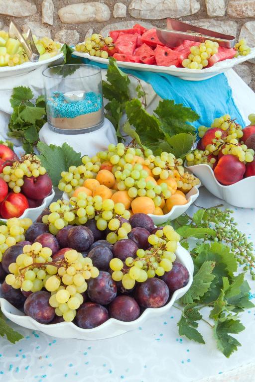 Svaigi augļi un vīnogas dekoratīvos traukos, papildināti ar lapām un dekoratīvu elementu. Ideāls galds vasaras svinībām.