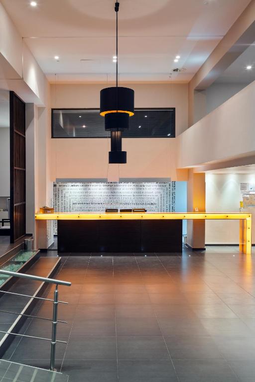 Mūsdienīgs viesnīcas reģistratūras dizains ar melnu un dzeltenu apgaismojumu, kas rada elegantu atmosfēru. Telpa ir plaša ar modernām apdares elementiem un logu, kas nodrošina dabisko apgaismojumu.