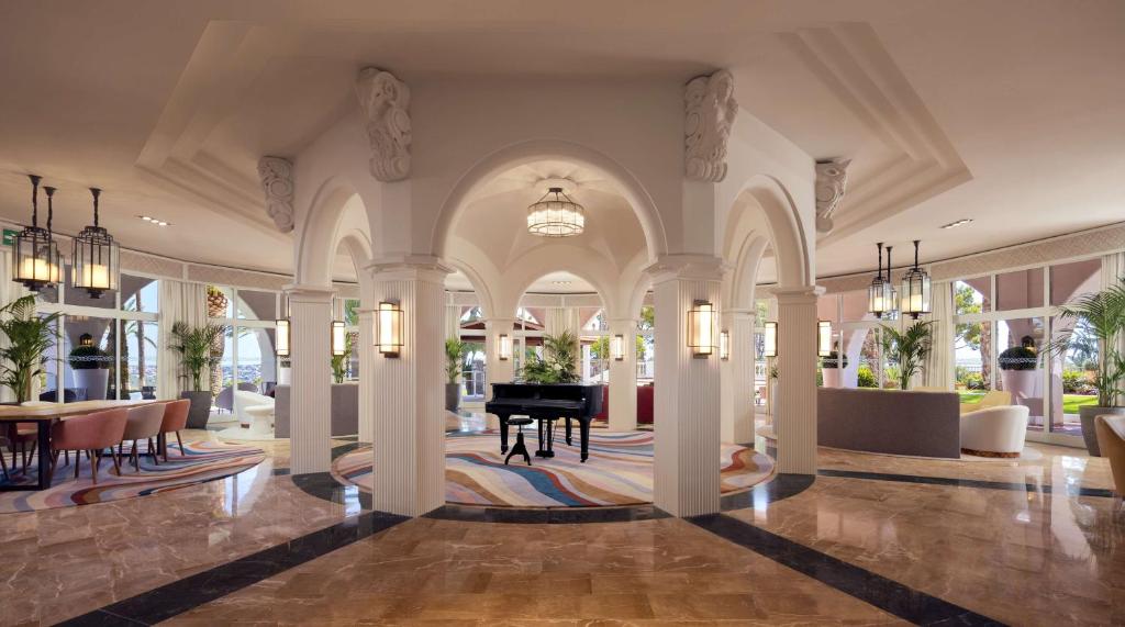 Eleganta viesnīcas halle ar arku un mūzikas instrumentu, kas papildina greznību un komfortu, nodrošinot patīkamu atmosfēru apmeklētājiem.