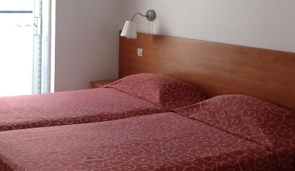 Guļamistaba ar diviem gultām, apklātām ar sarkanu rakstainu gultasveļu, un pie sienas piestiprināta lampiņa. Logu atvēršana nodrošina dabīgu apgaismojumu.