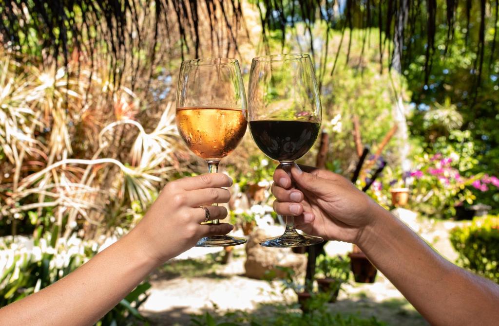 Sarkano un rozā vīna glāzes tiek paceltas sveicienā tropiskā dārzā, apņemot zaļumu un ziedus.