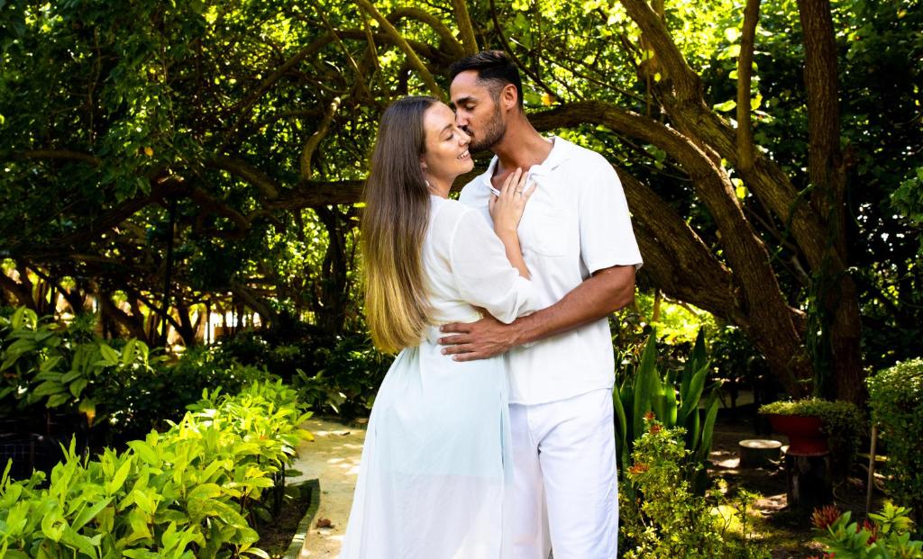 Mīlestības brīdis pāri skaistā dārzā, kur pāris apmainās siltām skūpstiem un skatieniem. Daba apkārt rada romantisku atmosfēru.