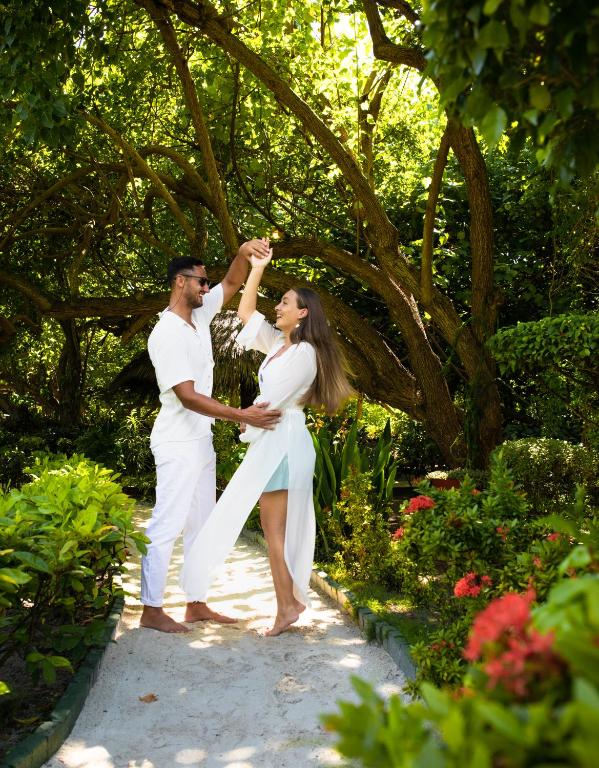 Pāris dejo dabas vidē, tērpti baltos apģērbos, ar laimīgām sejām un saulainu atmosfēru, apzaļumotā dārzā.