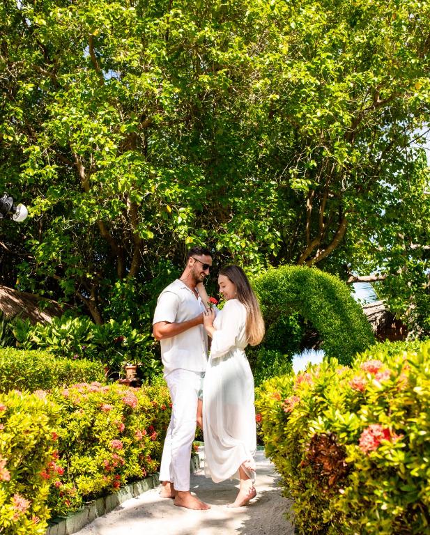 Jaunais pāris romantiskā brīdī dārzā, apstādījumos ar ziediem un zaļām lapām, bauda viens otra klātbūtni.