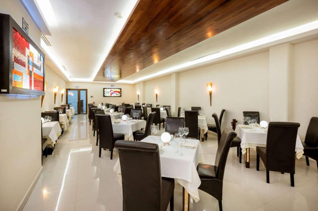 Mūsdienīgs restorāns ar elegantiem galdiem un krēsliem, kas izveidots gaišā interjerā. Uz sienas redzams mākslas darbs, kas piešķir telpai unikālu raksturu.