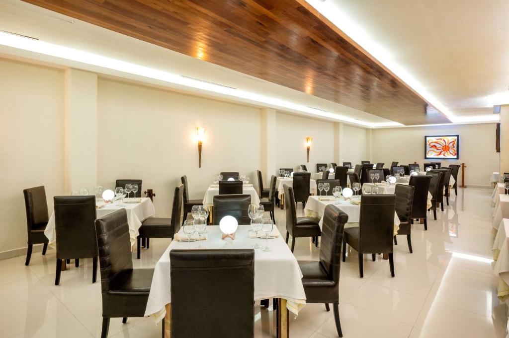 Mūsdienīgs restorāns ar elegantiem galdiem un krēsliem, kas izkārtoti gaišā telpā, kurā ir stilīgas apgaismojuma ierīces un dekoratīva māksla uz sienām.