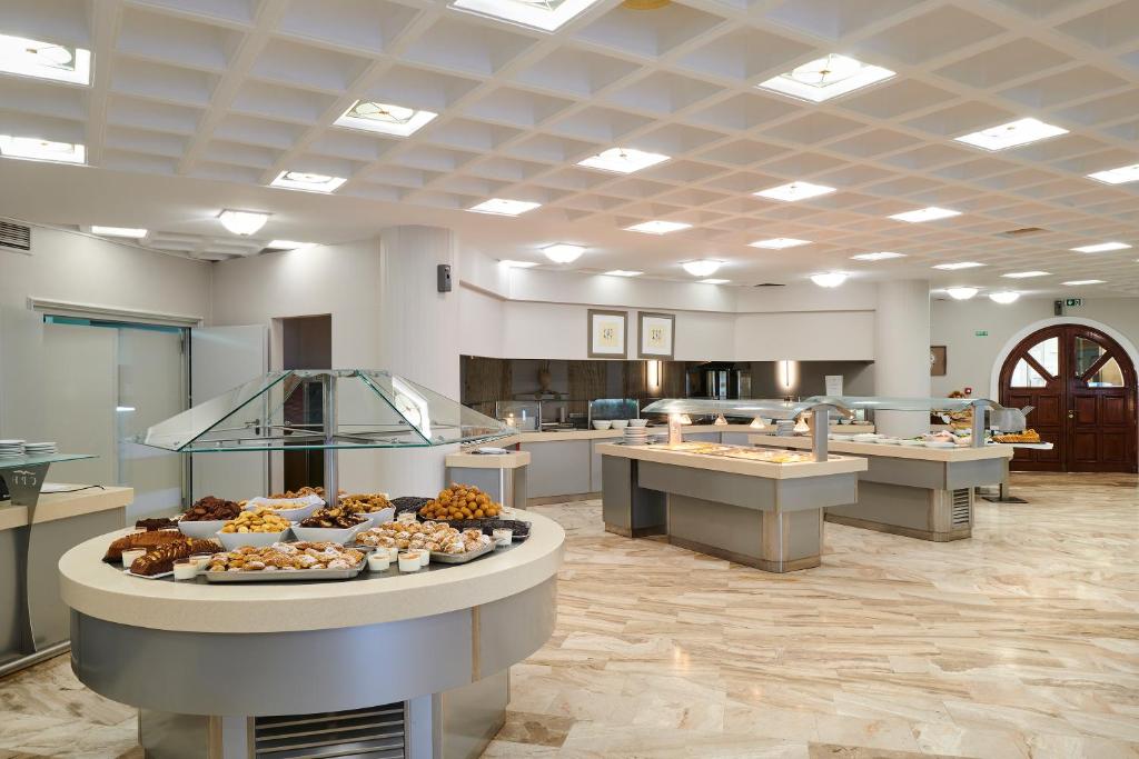 Moderns viesnīcas brokastu bufete ar plašu desertu un uzkodu izvēli, eleganti noformēta ar gaišiem toņiem un stikla akcentiem.