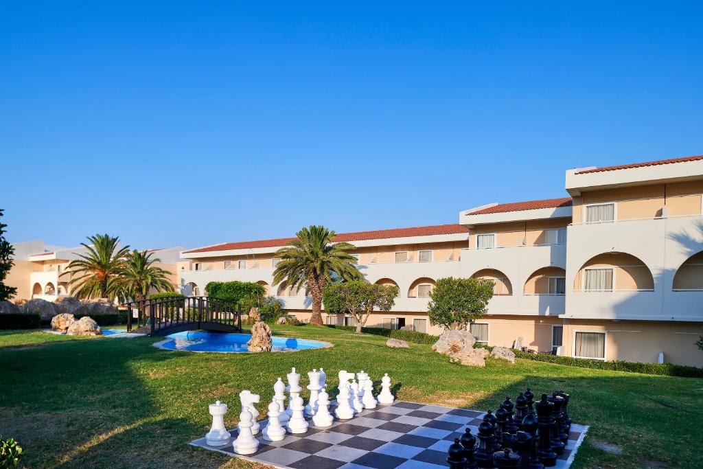 Viesnīcas dārzs ar lielu šaha komplektu, peldbaseinu un palmām, kas iepriecina saulainu dienu. Fons veido modernu arhitektūru un zaļumus.