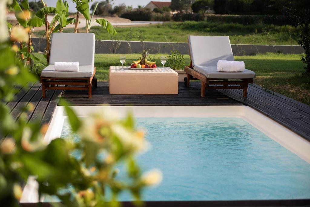 Mierīga atpūtas vieta ar divām sauļošanās krēslām pie baseina, kuru rotā augļi un dzērieni uz galda. Apkārtne ir zaļa un klusa, piedāvājot ideālu atmosfēru relaksācijai.