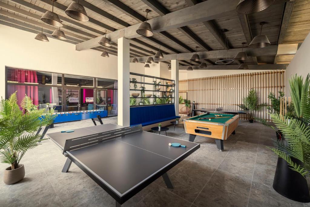 Mūsdienīga spēļu telpa ar galda tenisu, biljardu un dažādām izklaides iespējām, ko ieskauj augi un stilīgas apgaismojuma lampas.