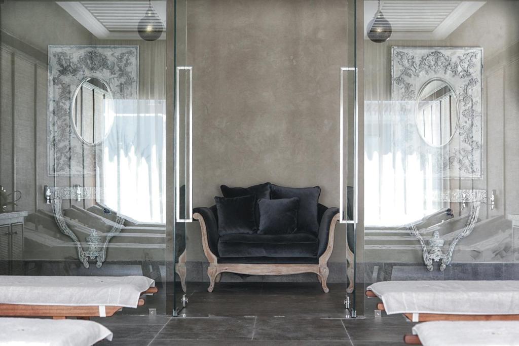 Mūsdienīga un eleganta atpūtas telpa ar melnu dīvānu un stikla sienām, kas rada gaisīgu atmosfēru. Interjerā redzamas dekoratīvas detaļas un spoguļi, kas piešķir telpai stilīgu izskatu.