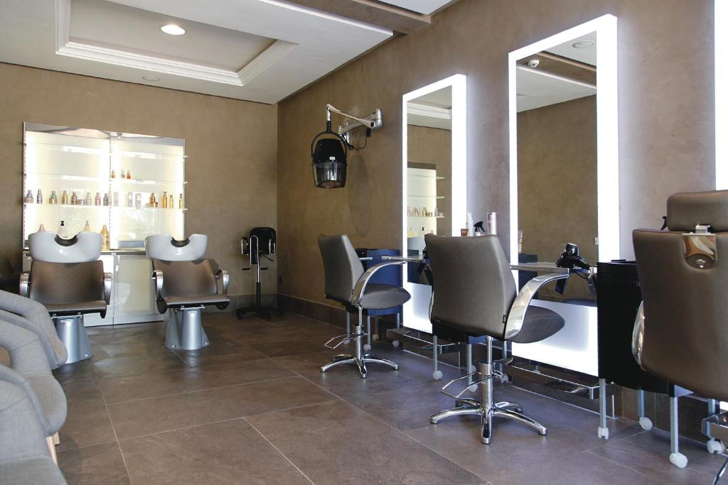 Mūsdienīgs frizētavas interjers ar elegantām spoguļiem, stilīgām krēslām un apgaismojumu. Skats uz frizētavas produktu plauktiem.