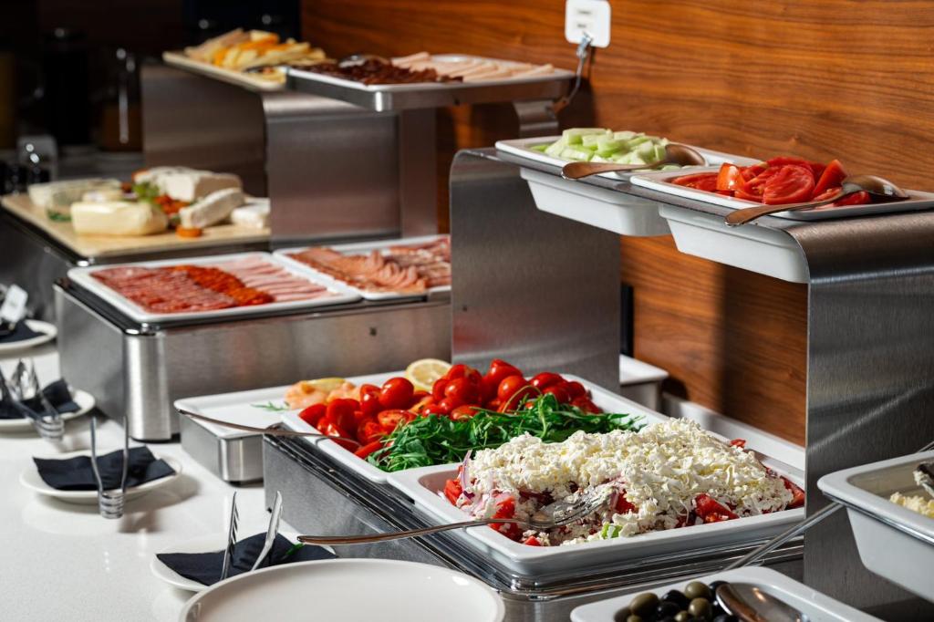 Bufete ar dažādiem ēdieniem, tostarp salātiem, gaļām un sieriem, kas pasniegti metāla traukos. Ideāls attēls, lai ilustrētu viesmīlību un ēdienu dažādību.