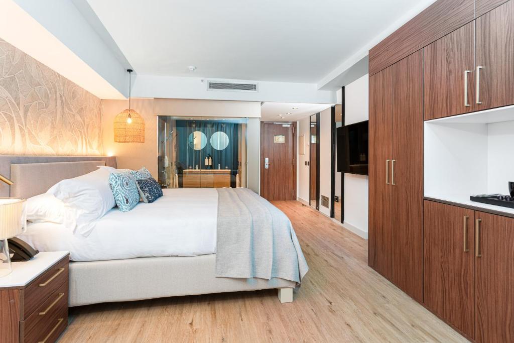 Mūsdienīga viesnīcas numura interjers ar ērku gultu, koka grīdu un modernām mēbelēm. Gaismas elementi un stikla duša piešķir telpai eleganci un komfortu.