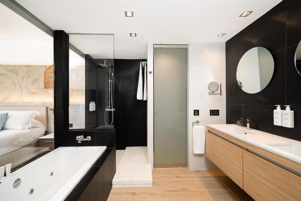 Mūsdienīgs vannas istabas interjers ar melnām flīzēm, stikla dušu un koka izlietni. Vannas istaba ir gaiša un eleganta, ar mūsdienīgiem apgaismojuma risinājumiem.