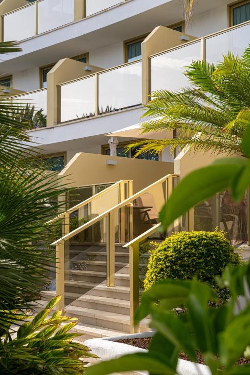 Modernas viesnīcas ieeja ar stikla margām un zaļiem augiem apkārt. Relaksējoša atmosfēra ar fokusēšanu uz dabu un komfortu.