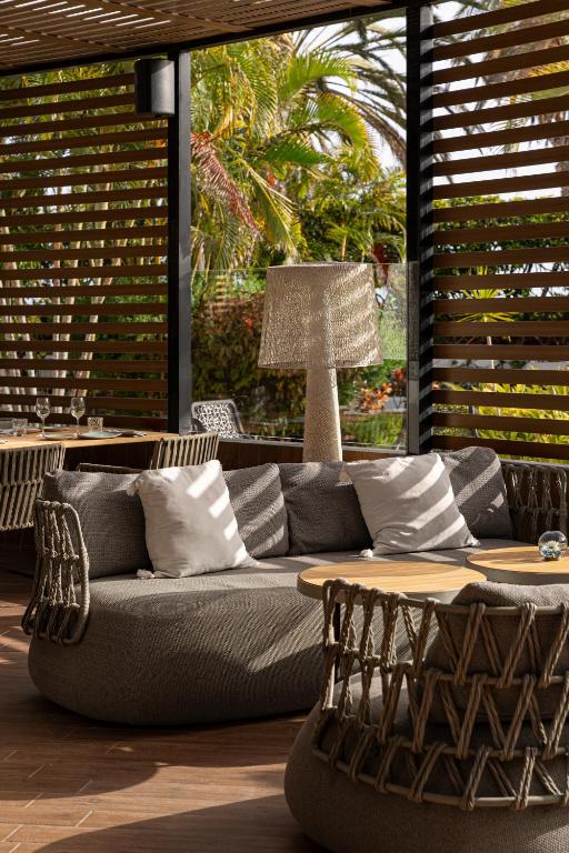 Mūsdienīgs interjers ar ērtiem dīvāniem un galdiem, kas atrodas telpā ar lieliem logiem, caur kuriem redzama zaļa daba. Gaismas lampa papildina relaksējošo atmosfēru.