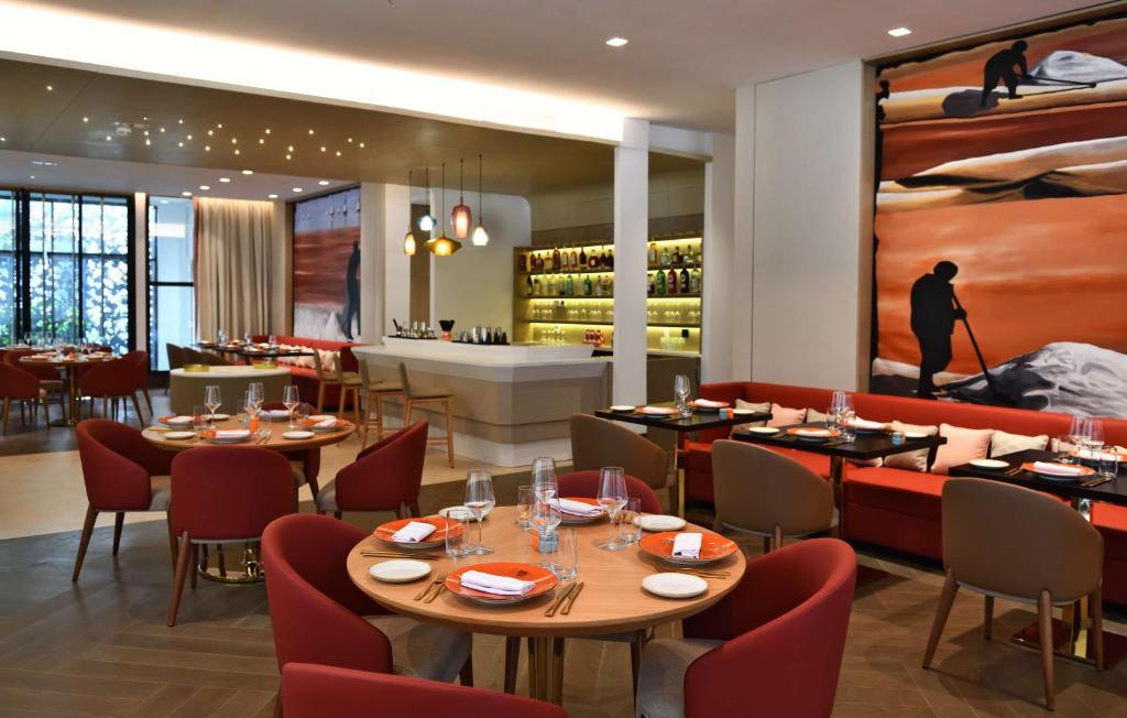 Mūsdienīgs restorāns ar elegantiem galdiem un krēsliem, kurā redzama stilīga bāra zona un mākslinieciska siena ar gleznām. Ideāla vieta relaksējošai maltītei un sociālai atmosfērai.