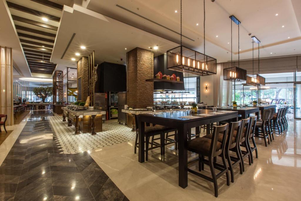 Mūsdienīgs restorāns ar elegantu interjeru, kas ietver garu ēdamgaldu un stilīgas gaismas. Telpa ir gaiša un plaša, radot patīkamu atmosfēru.