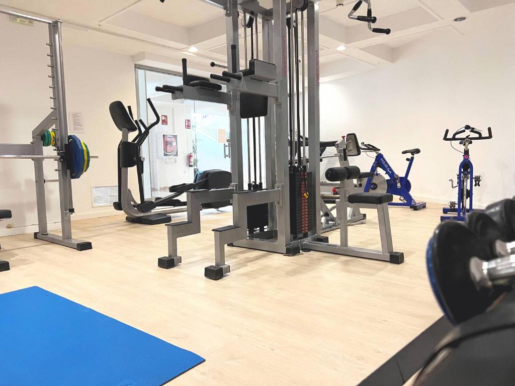 Mūsdienīgs sporta zāles interjers ar dažādām treniņu iekārtām, tostarp svara pacēlājiem un velotrenažieriem. Telpa ir gaiša un plaša, radot labvēlīgu vidi sportošanai.