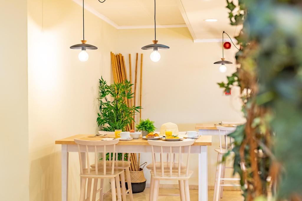 Gaiša un moderna restorāna iekārtojuma ainava ar koka galdu, ērtām krēslām un dekoratīvām zaļām augiem. Gaismas spuldzes pie griestiem rada patīkamu atmosfēru.