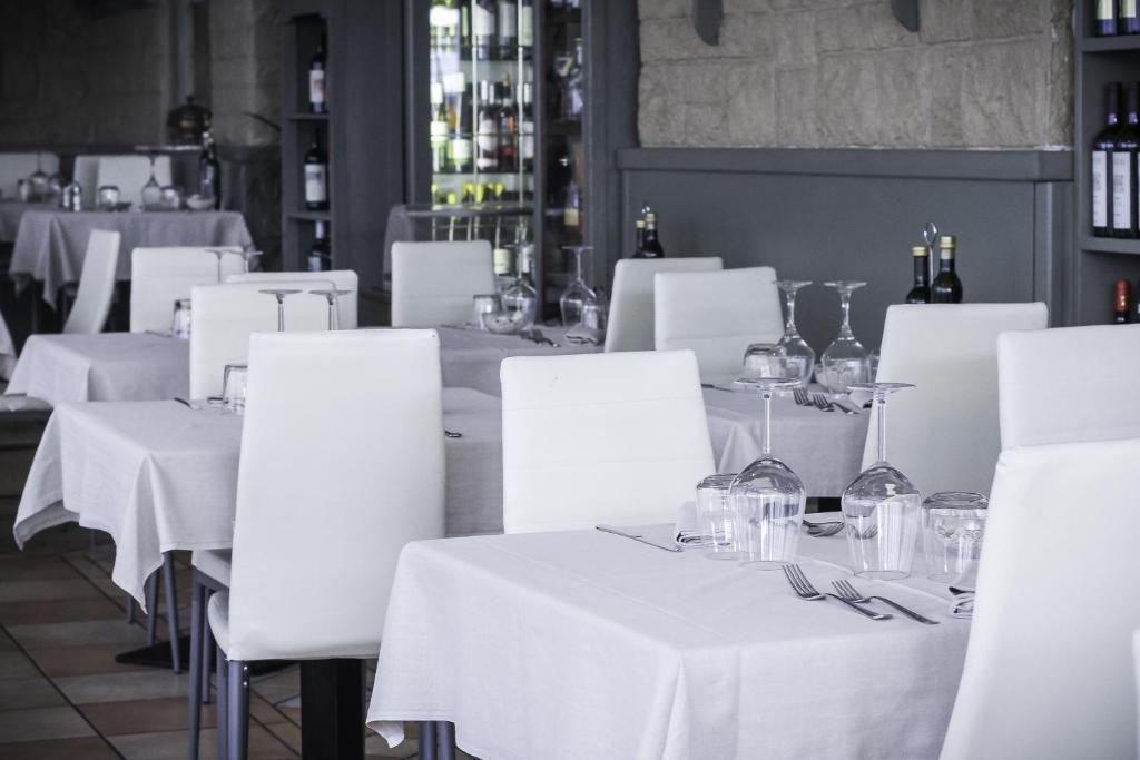 Gaišā un modernā restorāna iekārtojums ar baltām galda segām un elegantiem traukiem. Skats uz galdiem, kas gaida viesus, ar glāzēm un galda piederumiem.