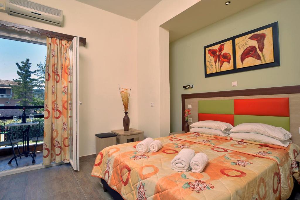 Mūsdienīgs guļamistabas interjers ar divguļamo gultu, krāsainām gultas segām un mākslas darbiem uz sienas. Logā redzama balkona zona ar galdu un krēsliem, kas nodrošina skatu uz ārpusi.