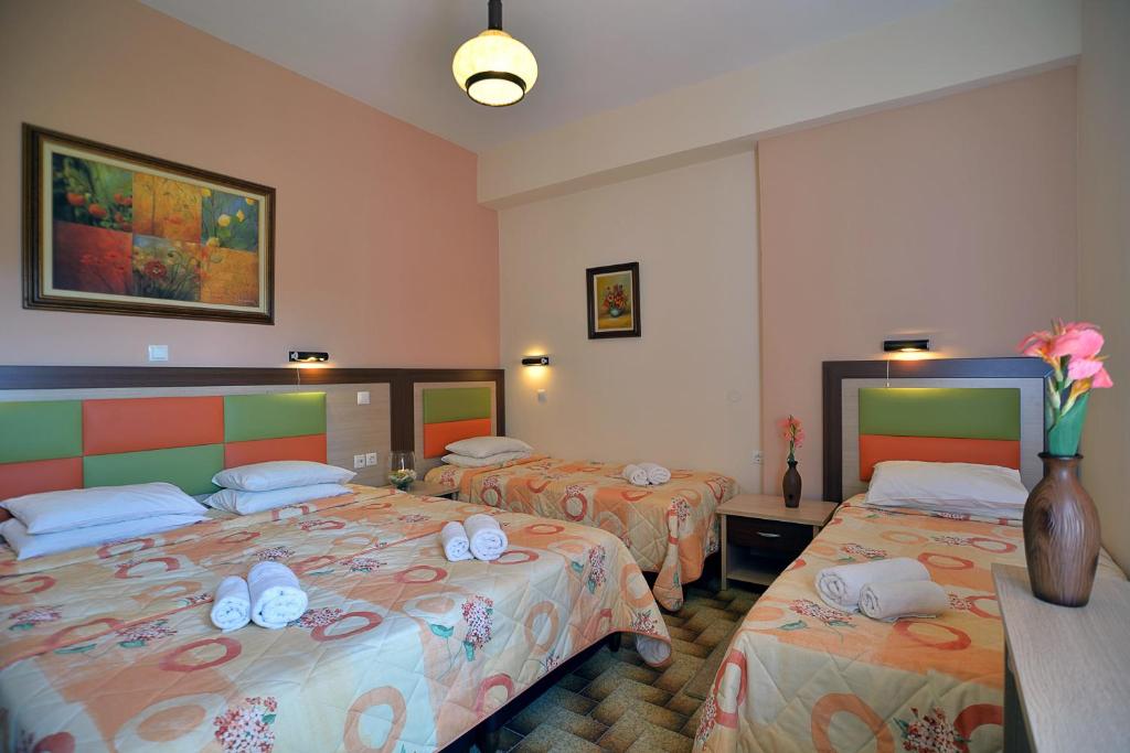 Mūsdienīga viesnīcas istaba ar divām gultām, dekorēta ar spilgtām krāsām un mākslas darbu sienā. Uz galda novietota vāze ar ziediem un dvieļi, kas sakārtoti uz gultām.