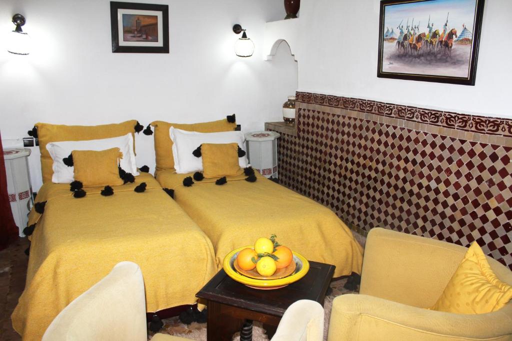 Gaiša guļamistaba ar divām gultām, kuras rotā dzeltenas segu un spilveni ar melniem pomponiem. Interjers ietver tradicionālu flīžu sienu un mākslas darbu, radot siltu un viesmīlīgu atmosfēru.