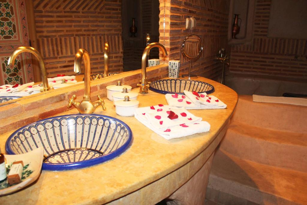 Elegants vannas istabas interjers ar zeltainām jaucējkrāniem, māksliniecisku izlietni un rožu ziedlapiņām uz dvieļiem. Sienas ir izstrādātas ar ķieģeļu rakstu, radot siltu atmosfēru.