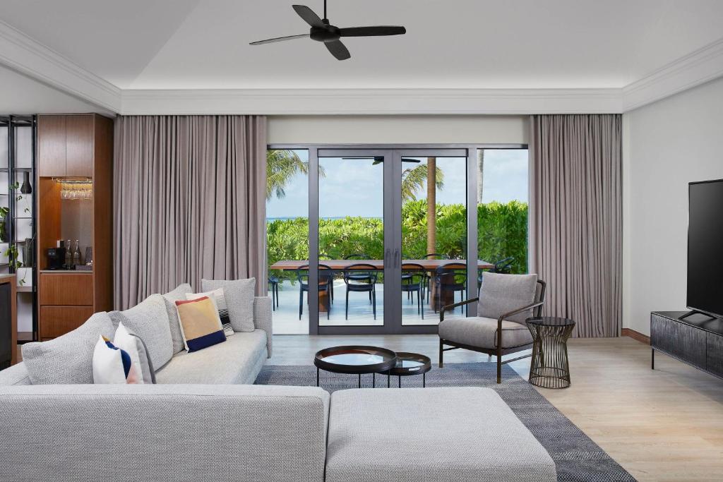 Mūsdienīgs viesistabas interjers ar atvērtu skatu uz dārzu. Gaiši pelēks dīvāns un eleganta ēdamzona pie loga, kurā ienāk dabiska gaisma.