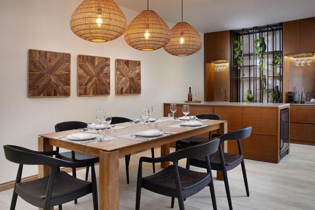 Mūsdienīgas ēdamistabas interjers ar koka galdu, melnām krēsliem un rotājumiem uz sienas. Gaismas ķermeņi rada siltu atmosfēru, savukārt augu akcenti piešķir dzīvīgumu telpai.