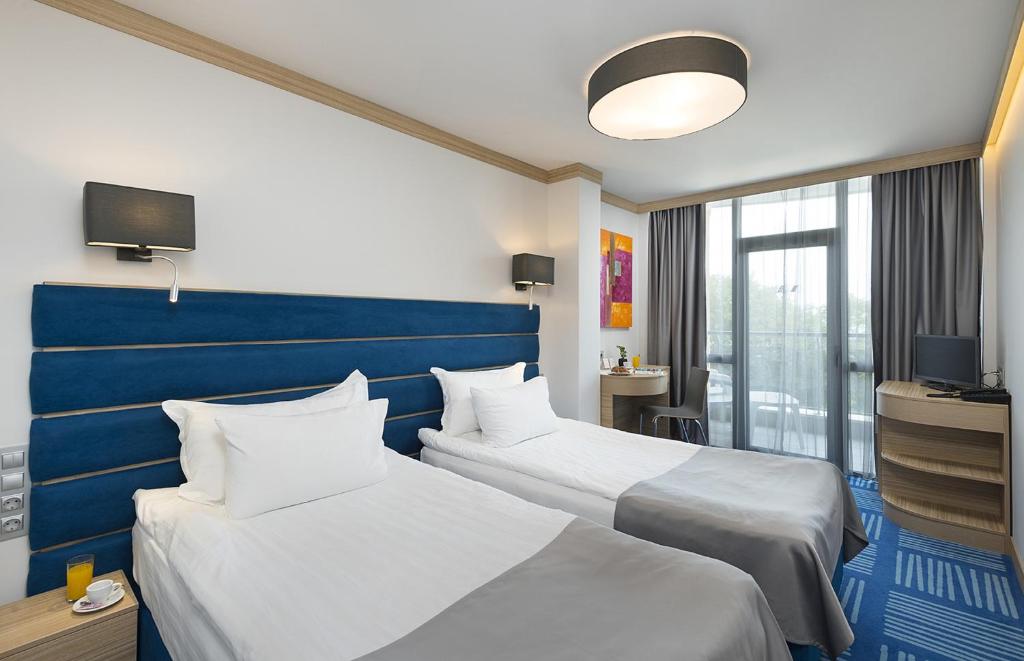 Mūsdienīga viesnīcas numura iekārtojums ar divām atsevišķām gultām, zilu galvgalvi un gaišiem aizkariem. Numurā ir rakstāmgalds un televizors, kā arī balkons, kas nodrošina skatu uz ārpusi.