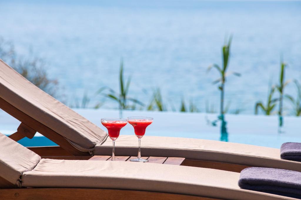 Divas kokteiļu glāzes ar sarkanu dzērienu atpūtas krēslā pie baseina ar skatu uz jūru. Ideāla ainava relaksācijai un brīvā laika pavadīšanai.
