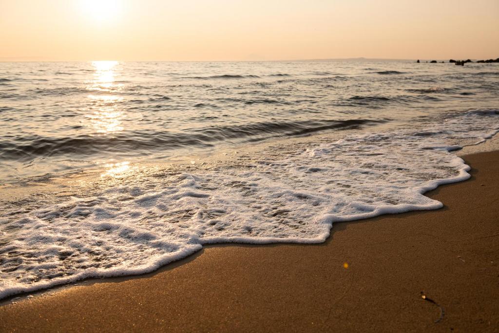 Saulrieta gaisma atspoguļojas jūrā, viļņi maigi plūst uz pludmali, radot burbuļus smiltīs. Šī ainava rada mierīgu un relaksējošu atmosfēru.