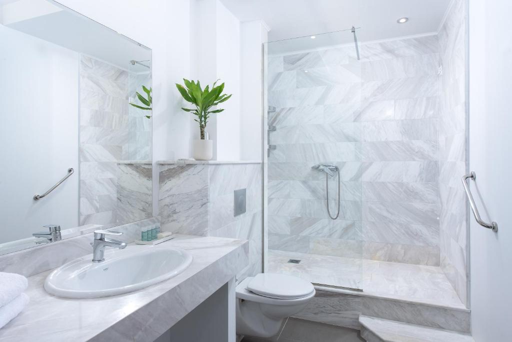 Mūsdienīga vannas istaba ar marmora apdari, dušu ar stikla durvīm un minimālistisku dizainu, kas ietver zaļu augu un higiēnas piederumus.