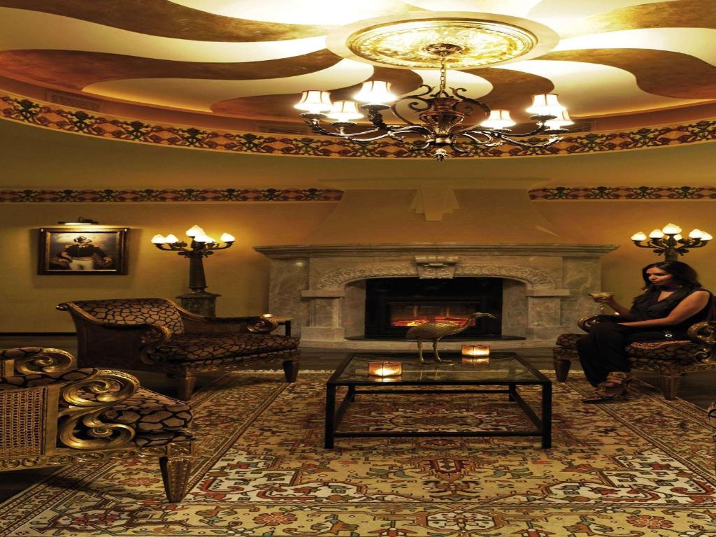 Elegants interjers ar greznām mēbelēm un kamīnu, kas rada siltu un aicinošu atmosfēru. Telpas centrā ir stikla galdiņš ar svečturiem, un uz sienas ir mākslas darbs.