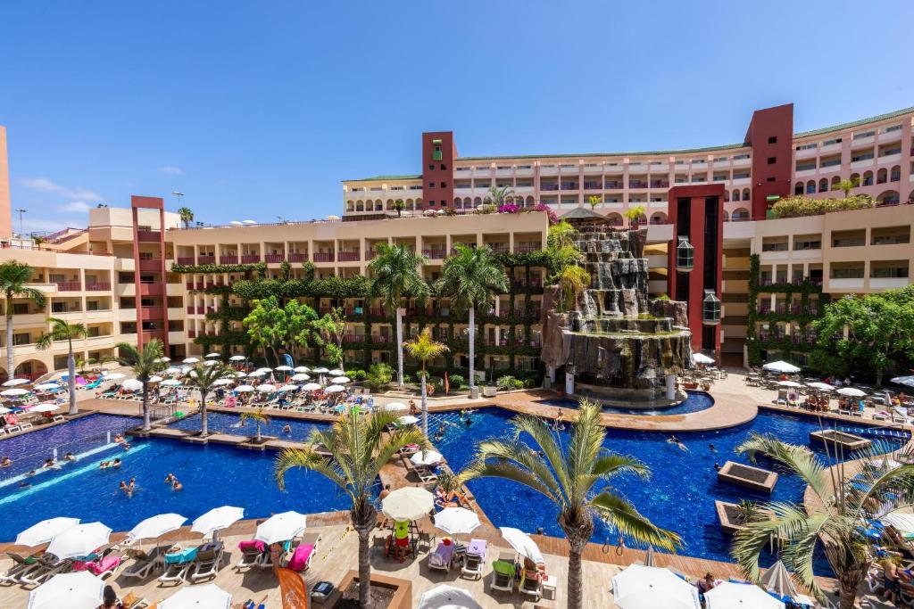 Viesnīcas baseins ar ūdens kritumu un saulainu apkārtni, apņemts ar palmām un sauļošanās krēsliem. Ideāla vieta atpūtai un relaksācijai.