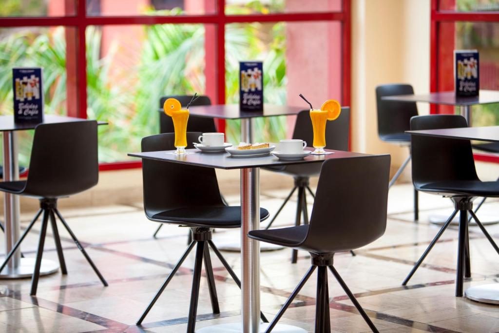 Mūsdienīga kafejnīca ar melnām krēsliem un galdiem, uz kuriem atrodas dzērieni un kafija. Logi ar sarkanu rāmi nodrošina dabiska apgaismojuma plūsmu un skatu uz zaļumiem.